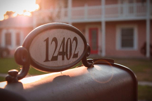 a close up of the house number 12402 mounted on top of a mailbox in the background a pink house with a white balcony can be seen